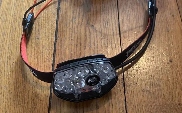 La frontale Petzl Nao RL posée sur un parquet, vue de face, avec ses LED et son bandeau rouge